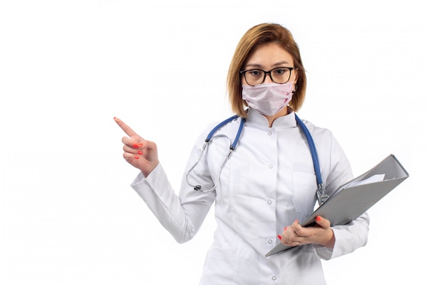 Foto gratuita joven doctora en traje médico blanco con estetoscopio en máscara protectora blanca con archivos en el blanco