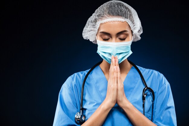 Joven doctora en uniforme haciendo gesto de oración aislado