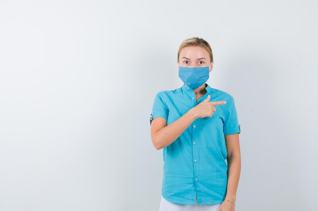 Joven doctora en uniforme médico, máscara apuntando hacia el lado derecho