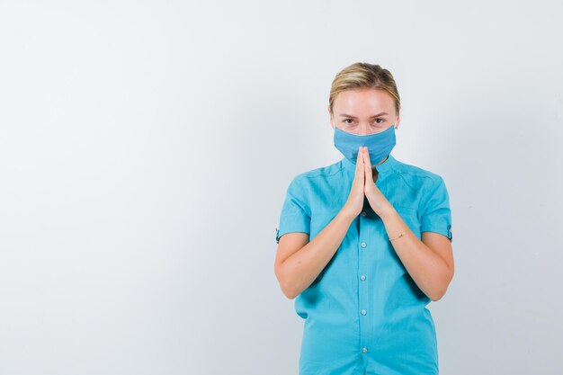 Joven doctora en uniforme mostrando las manos juntas en gesto de súplica aislado