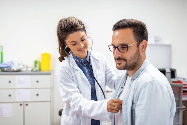 Foto gratuita joven doctora está usando un estetoscopio para escuchar los latidos del corazón del paciente toma de una doctora dándole un chequeo a un paciente varón