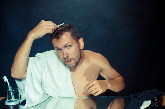 Foto gratuita joven en el dormitorio sentado frente al espejo rascándose la barba