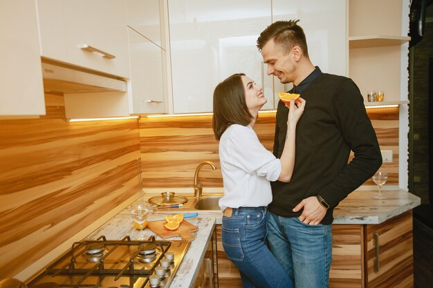 joven y dulce pareja encantadora de pie en la cocina con naranja