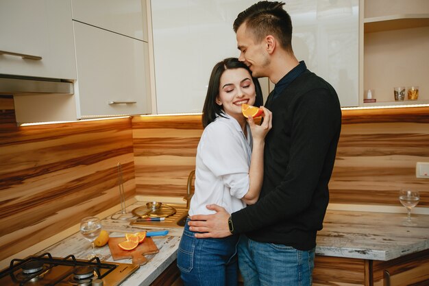 joven y dulce pareja encantadora de pie en la cocina con naranja