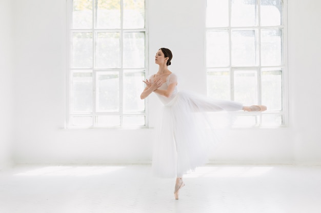 Joven e increíblemente bella bailarina está posando y bailando en un estudio blanco