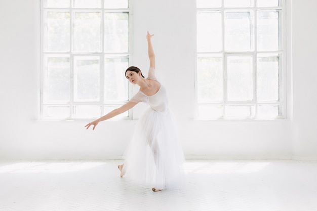 Joven e increíblemente bella bailarina está posando y bailando en un estudio blanco