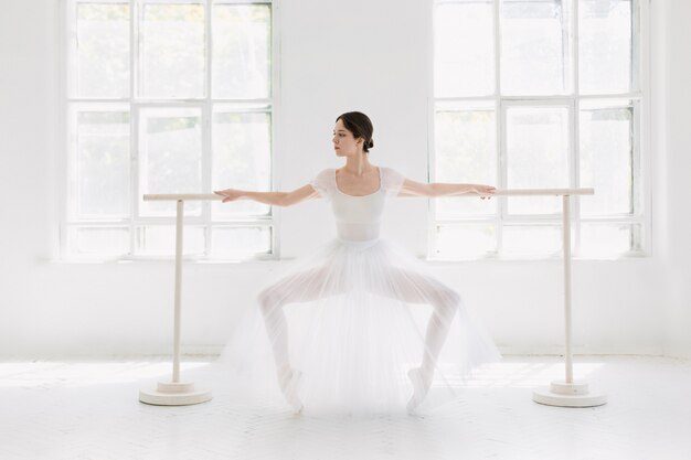 Joven e increíblemente bella bailarina está posando y bailando en un estudio blanco