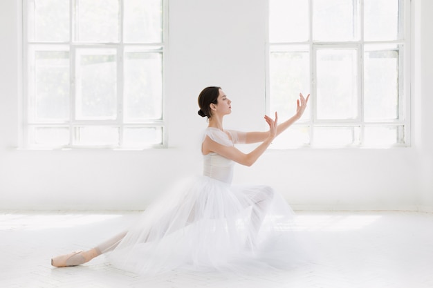 Joven e increíblemente bella bailarina está posando y bailando en un estudio blanco