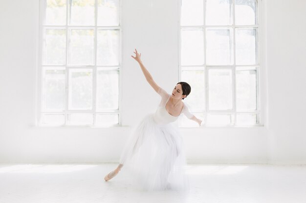 Joven e increíblemente bella bailarina está posando y bailando en un estudio blanco