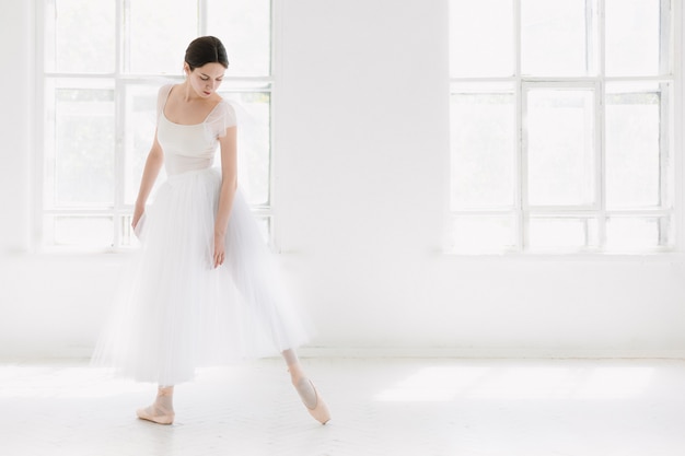 Foto gratuita joven e increíblemente bella bailarina está posando y bailando en un estudio blanco