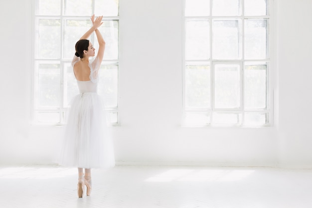 Joven e increíblemente bella bailarina está posando y bailando en un estudio blanco