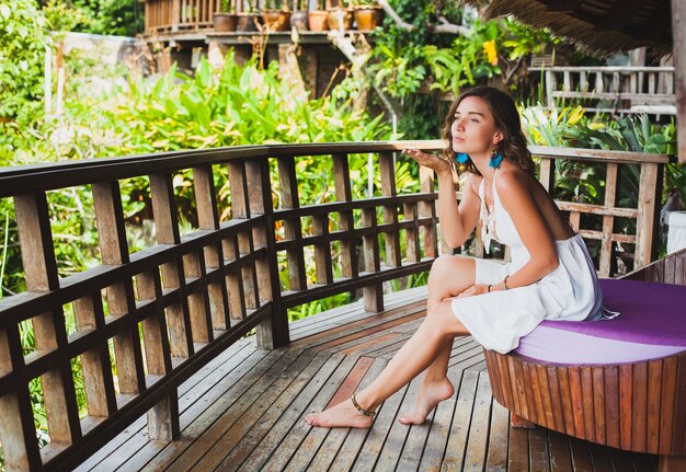 Joven e inocente mujer hermosa pura soñando, sentada en el sofá con vestido blanco, romántico, lírico, pensando, verde naturaleza tropical, verano, relajado, escalofriante, piernas, hotel resort