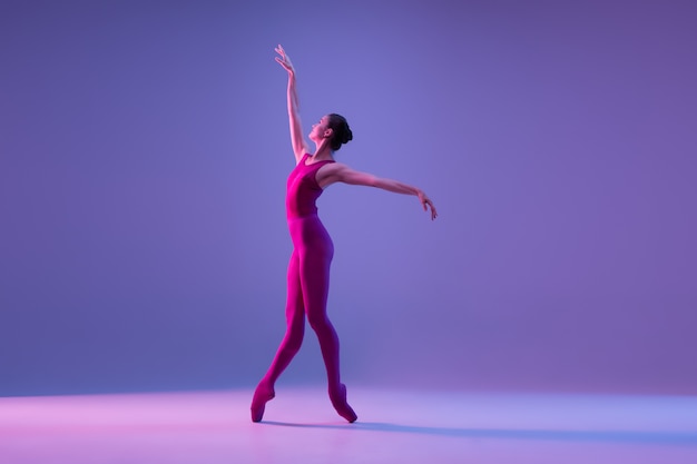 Joven y elegante bailarina de ballet aislada sobre fondo de estudio púrpura en luz de neón