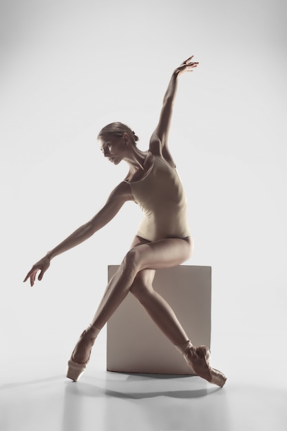 Joven elegante bailarina de ballet clásico o bailarina clásica bailando en estudio blanco.