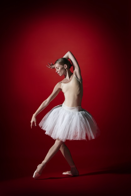 Joven elegante bailarina de ballet clásico o bailarina clásica bailando en el estudio rojo. modelo caucásico en zapatillas de punta