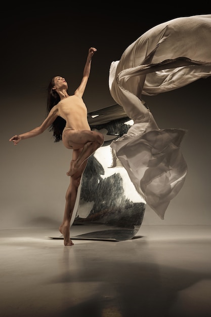 Joven y elegante bailarina de ballet moderno en pared marrón con espejo