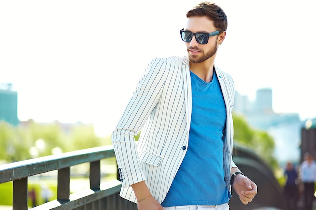 Joven elegante confiado feliz guapo empresario modelo en traje hipster ropa caminando en la calle con gafas de sol