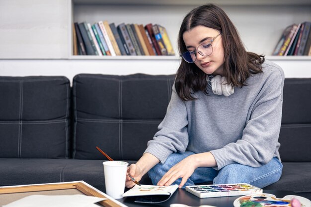 Una joven elegante dibuja con pinturas en el interior de la casa