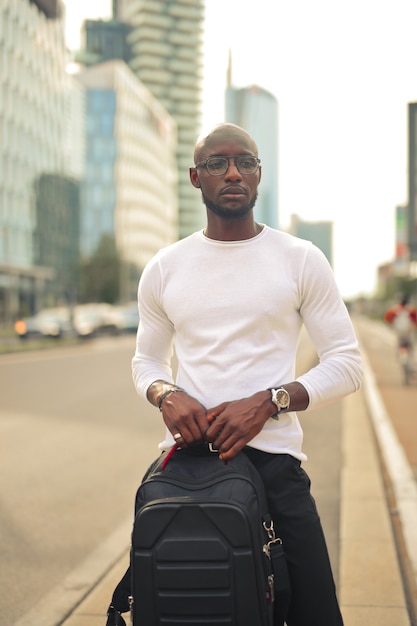 Joven elegante con gafas sosteniendo una mochila en la calle bajo la luz del sol