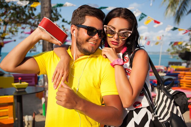 Foto gratuita joven elegante hipster hermosa pareja en vacaciones de verano en tailandia, coqueta, atuendo de moda, gafas de sol, romance tropical, sonriente, feliz, escuchando música, humor de fiesta, café en la playa