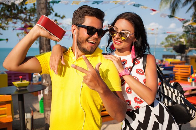 Joven elegante hipster hermosa pareja en vacaciones de verano en Tailandia, coqueta, atuendo de moda, gafas de sol, romance tropical, sonriente, feliz, escuchando música, humor de fiesta, café en la playa