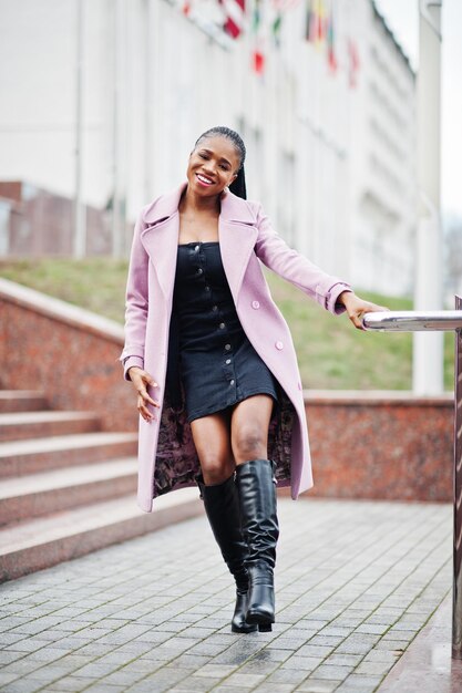 Joven y elegante mujer afroamericana en la calle con abrigo de moda contra banderas de diferentes países del mundo