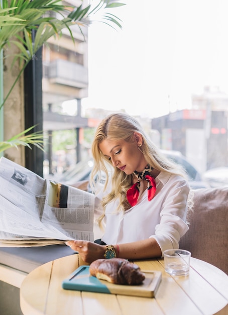 Foto gratuita joven elegante mujer leyendo el periódico en la cafetería