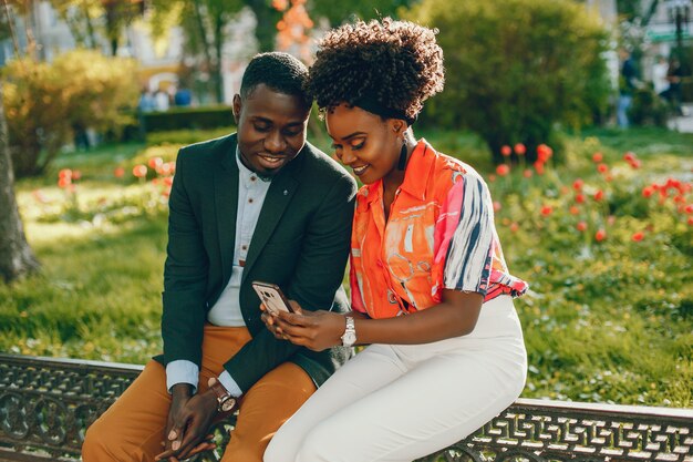 Una joven y elegante pareja de piel oscura sentada en una ciudad soleada y usa el teléfono