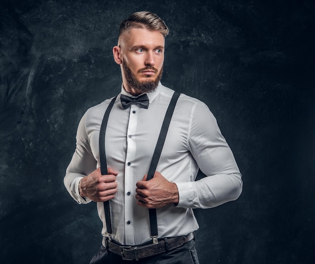 Foto gratuita joven elegantemente vestido con camisa con pajarita y tirantes. foto de estudio contra un fondo de pared oscuro