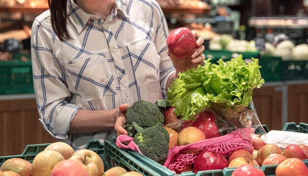 Una joven elige frutas y verduras en un supermercado.