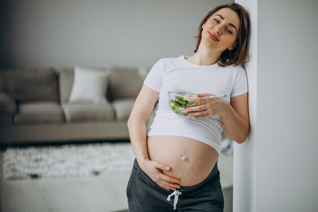 Joven embarazada comiendo ensalada en casa