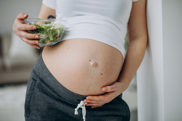 Joven embarazada comiendo ensalada en casa