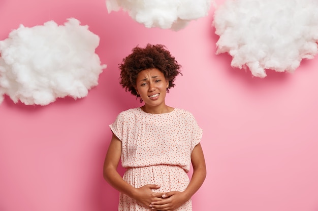 Joven embarazada descontenta se siente mal por las contracciones, se toca la barriga y tiene calambres, sufre de dolor abdominal, va a dar a luz, se prepara para la paternidad. Futura madre