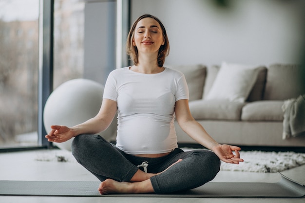 Joven embarazada practicando yoga en casa