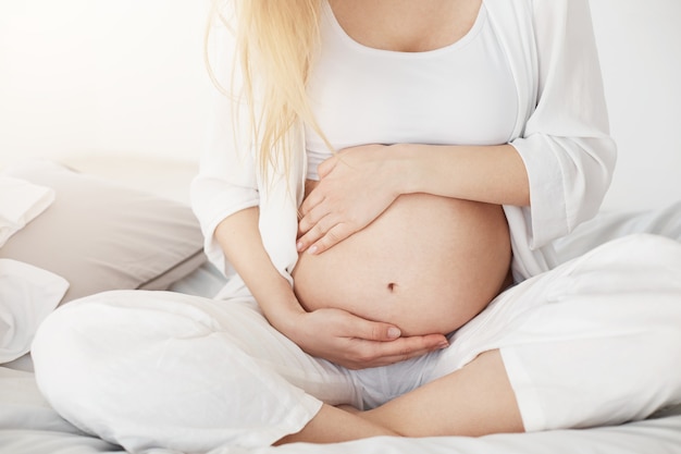 Joven embarazada que pronto será madre tocando su vientre sentado en su dormitorio por la tarde. Concepto de embarazo.