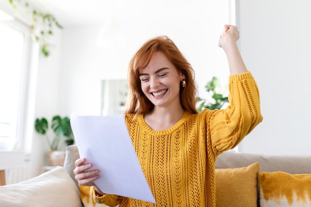 Una joven emocionada sostiene una carta en papel y se siente eufórica al recibir un ascenso laboral o un reembolso de impuestos del banco. Una mujer feliz leyendo un documento de papeleo sonriendo de buenas noticias agradables obteniendo una beca para estudiantes.