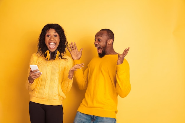 Joven emocional afroamericano y mujer en ropa casual brillante en espacio amarillo. Hermosa pareja