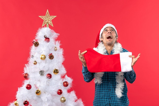 Joven emocional con sombrero de santa claus en una camisa azul a rayas y sosteniendo un calcetín de navidad mirando arriba