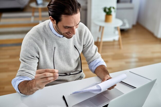 Joven emprendedor feliz trabajando en casa y analizando informes comerciales