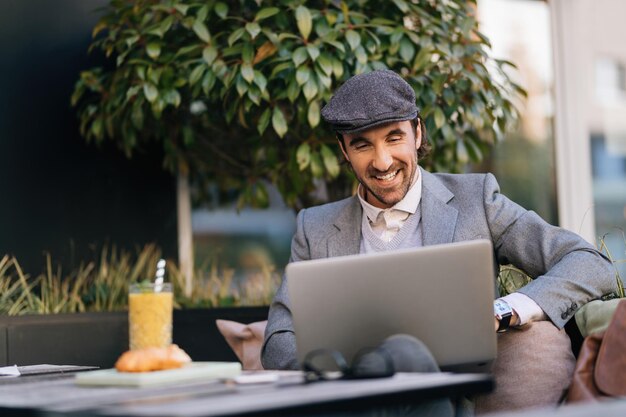 Joven emprendedor feliz trabajando en una laptop mientras se relaja en un café al aire libre