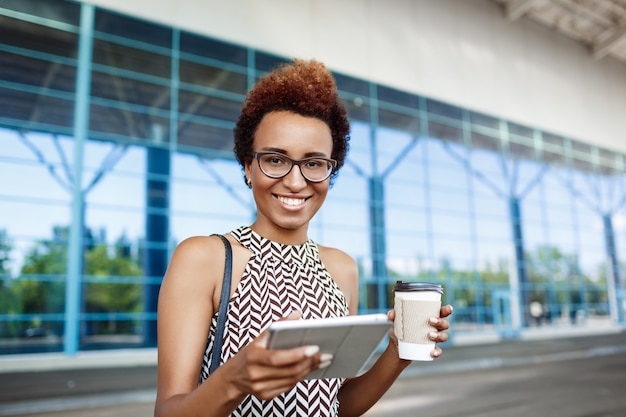 Joven empresaria africana exitosa en gafas de pie cerca del centro de negocios.