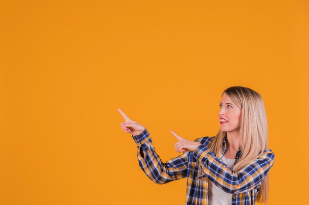 Una joven empresaria apuntando sus dedos contra un fondo naranja