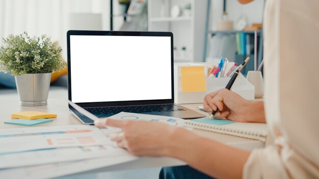 Joven empresaria de Asia utiliza un teléfono inteligente con pantalla en blanco mientras trabaja de forma inteligente desde casa en la sala de estar