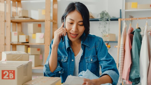 Joven empresaria asiática que usa un teléfono inteligente que recibe la orden de compra y verifica el producto en el trabajo de stock en la oficina en casa