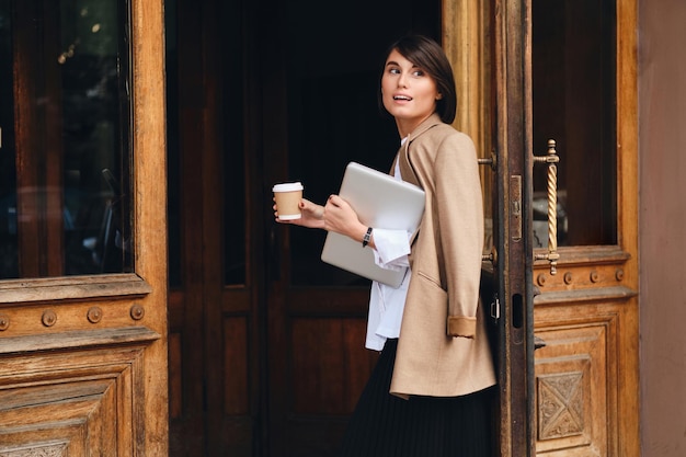 Joven empresaria atractiva y elegante con laptop y café para salir al aire libre