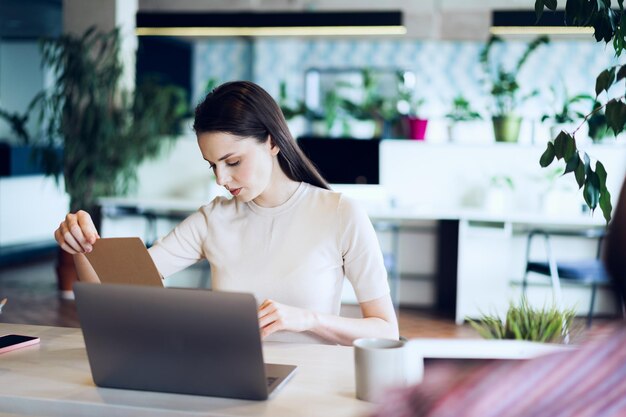 Joven empresaria atractiva haciendo notas en el bloc de notas en su lugar de trabajo