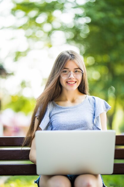 Joven empresaria atractiva se sienta en un banco del parque y trabaja en su cuaderno