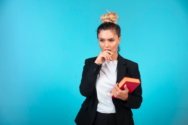 Joven empresaria en blazer negro sosteniendo un libro y pensando