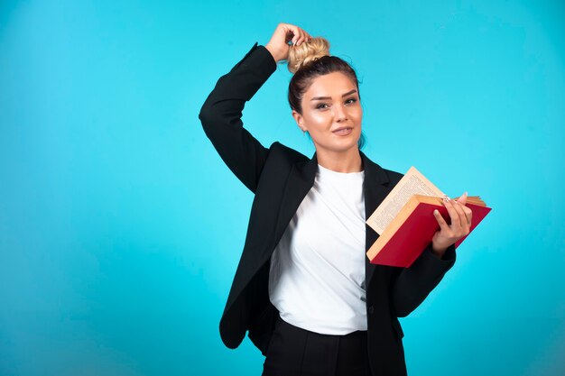 Joven empresaria en blazer negro sosteniendo un libro de tareas y comprobando su moño.