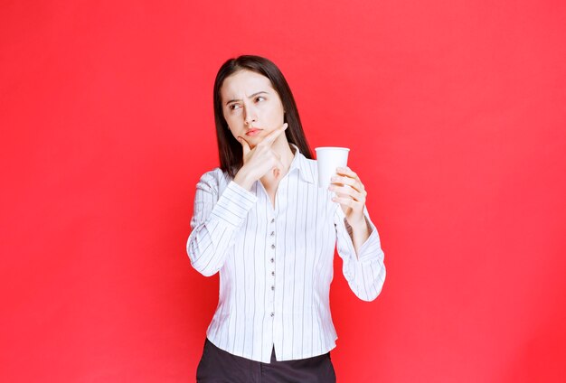 Joven empresaria bonita sosteniendo un vaso de plástico sobre fondo rojo.